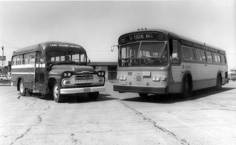 Two vintage transit buses parked side by side in a lot; one is an older, rounded model and the other a newer, larger model marked “53 Eugene-Mall.”.