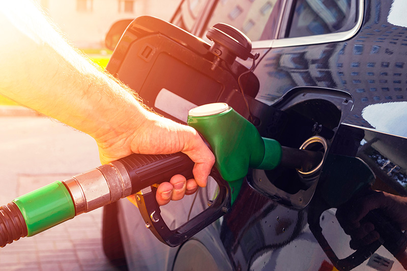 A person is refueling a car at a gas station, holding a green fuel nozzle inserted into the vehicle's gas tank.