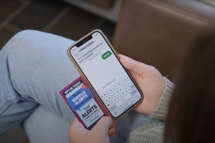 A person holding a mobile phone and a service alerts card, typing a text message to receive alerts.